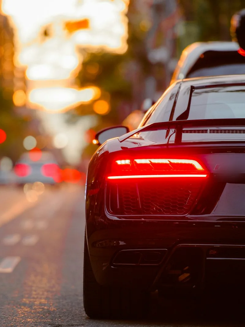 A sports car on a city street at dusk, tail lights glowing